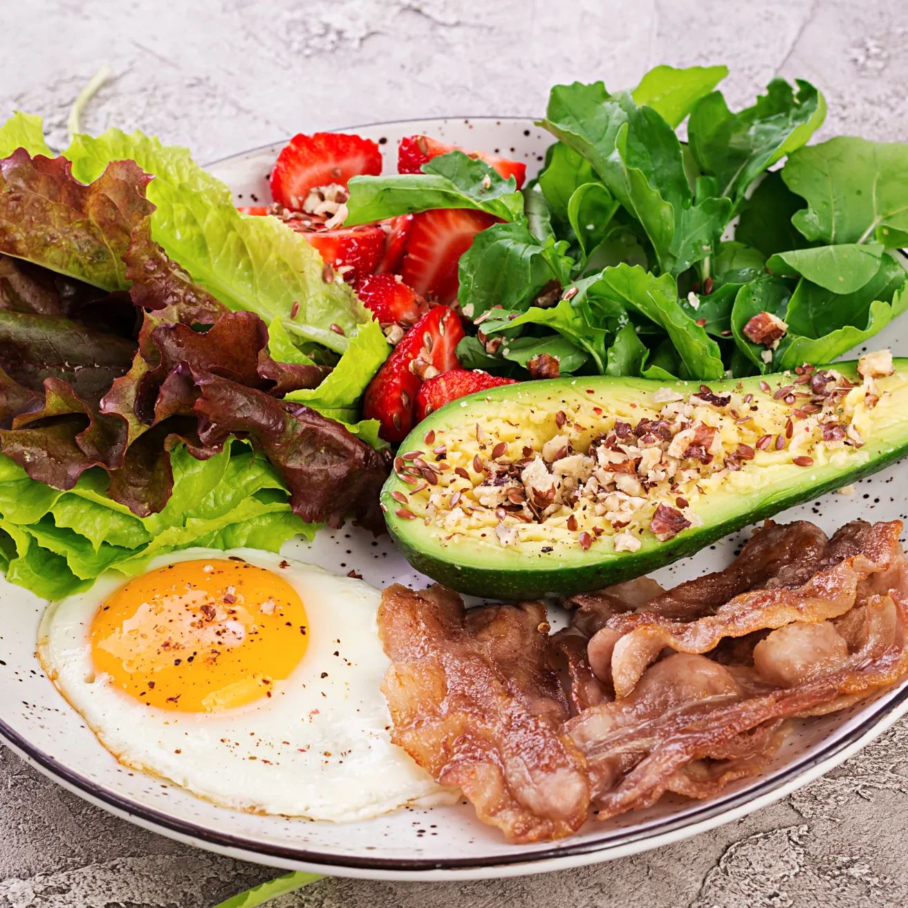 Keto recept: bord met gebakken ei, avocado met zaden, spek, sla en aardbeien